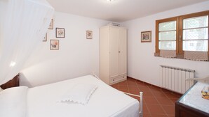 Quarto com cama, guarda-roupa, janela com cortinas de renda e radiador.