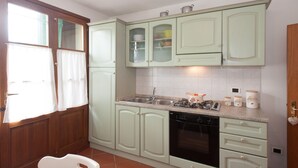 Uma cozinha com armários verde-claros, lava-louças, fogão e janela com cortinas.