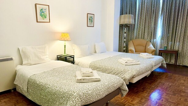 Une chambre d’hôtel avec deux lits, une chaise, une lampe et une fenêtre avec des rideaux.