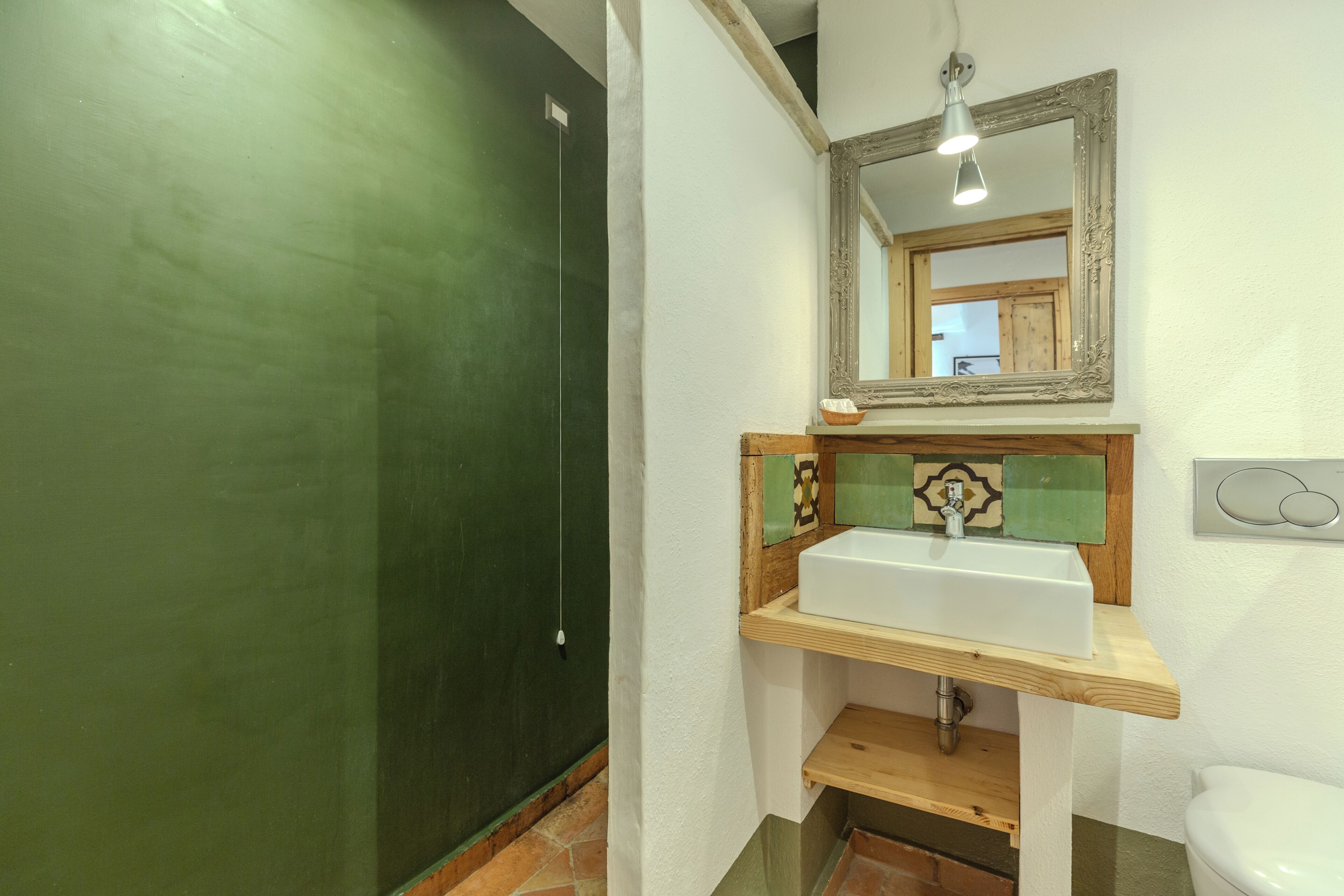 A bathroom with a green door, a white sink with a wooden countertop, a mirror with an ornate frame, and a light fixture above the mirror.