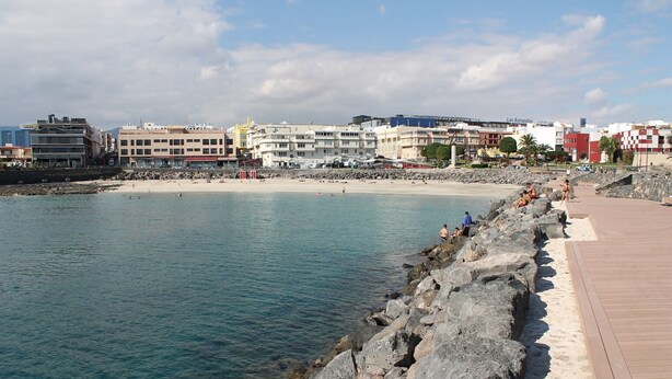 A coastal area with a rocky shoreline, a wooden boardwalk, and buildings in the background.