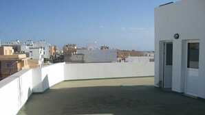 A rooftop terrace with a white wall and a door, overlooking a cityscape.