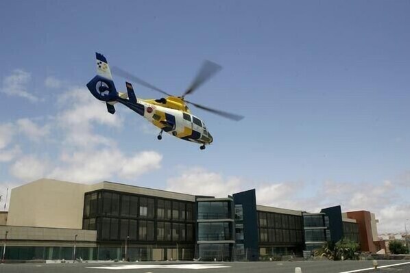 A helicopter flying in front of a modern building with large windows and a flat roof.