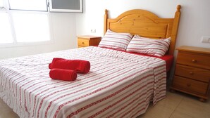 A neatly made bed with a patterned bedspread and two red towels, wooden nightstands, and a wooden headboard.