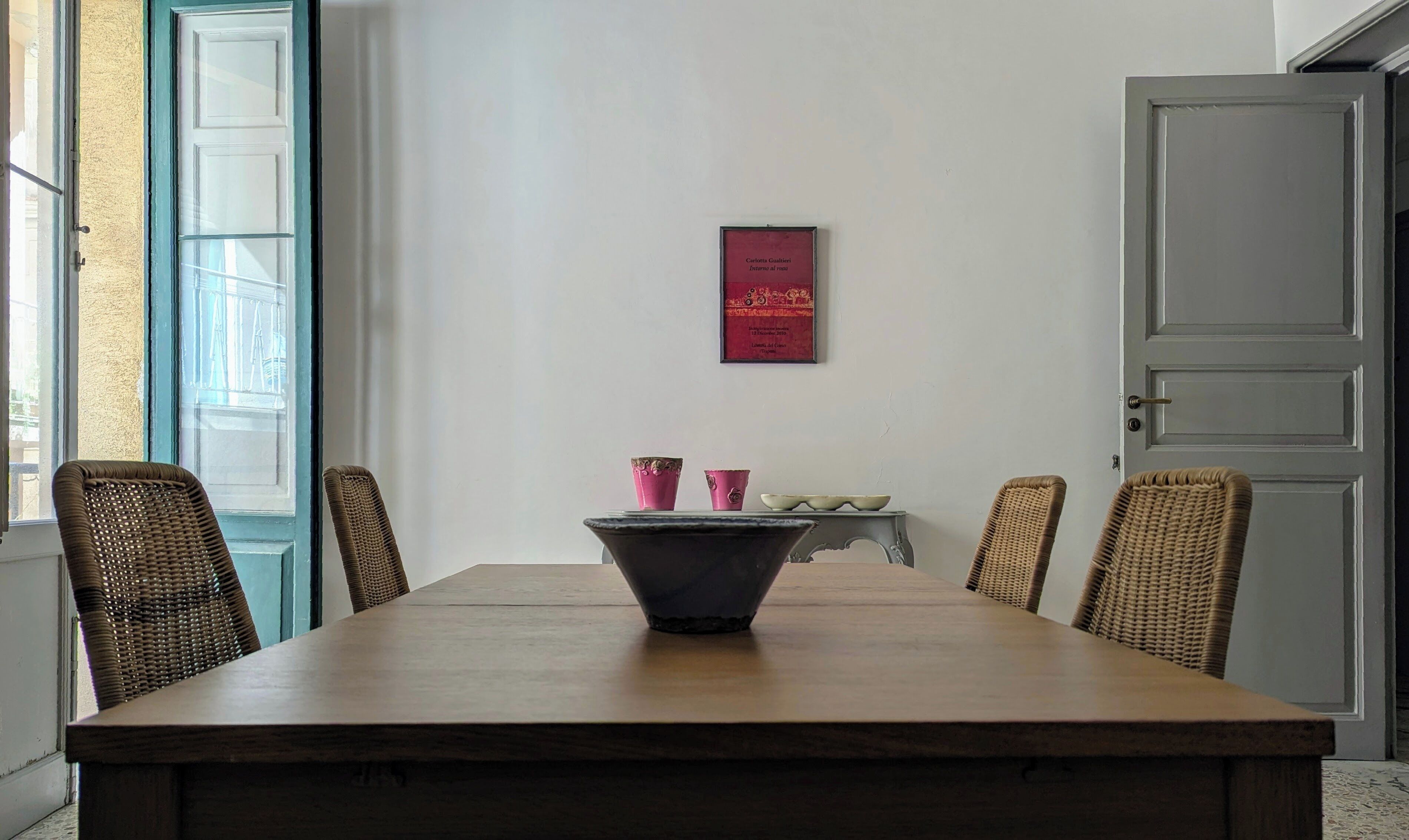 Ein Essbereich mit Holztisch, Korbstühlen und einem gerahmten Kunstwerk an der Wand.