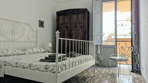 A bedroom with a white four-poster bed, a dark wooden wardrobe, a small table with a lamp, and a chair by the window.