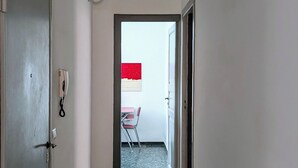 A hallway with a marble floor, a phone on the wall, and a door on the left.