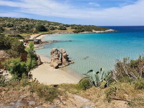 A coastal landscape with clear turquoise waters, rocky formations, and a sandy beach.