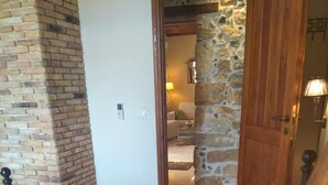 Camera da letto con parete in mattoni, porta in legno e vista su un'altra stanza con divano e lampada.