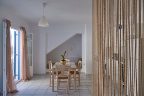 A dining area with a table, chairs, a hanging light fixture, and a staircase in the background.