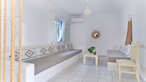 A white room with a sofa, a small table with a plant, a hanging light, and a mirror on the wall. - Dionysus | 2 Bedroom Family Apartment with Sea View and Patio, Cleopatra Homes P (Paros)