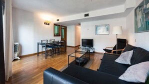 En moderne stue med en sort sofa, et spisebord med stole, et fjernsyn og en lampe.