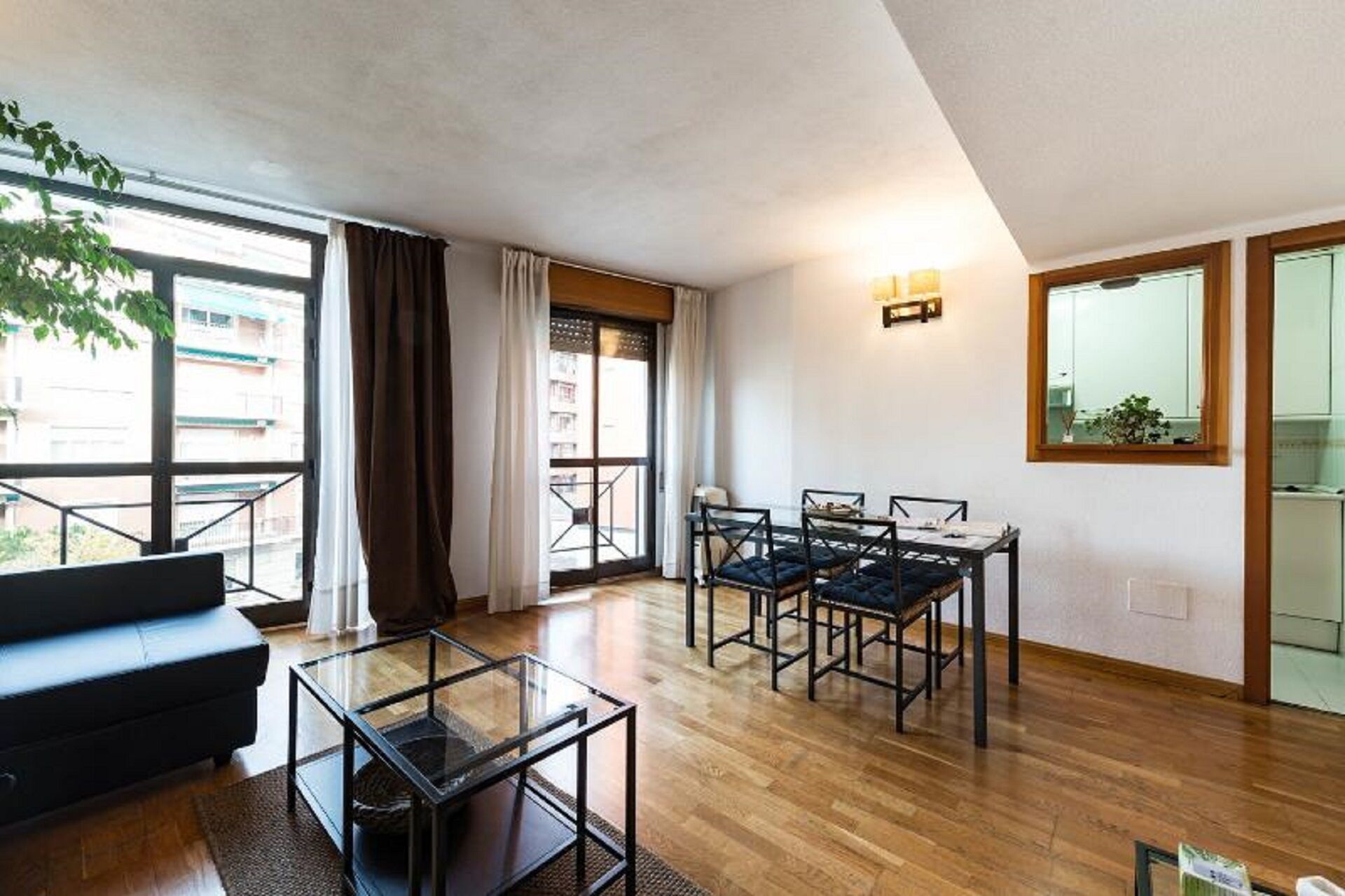 A modern living room with a sofa, a glass coffee table, and a dining area with four chairs.