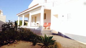 A white building with a covered porch, outdoor seating, and a garden area. - HOUSE OF THE DUNES - DONNALUCATA (Donnalucata)