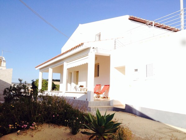 A white building with a covered porch, outdoor seating, and a garden area. - HOUSE OF THE DUNES - DONNALUCATA (Donnalucata)