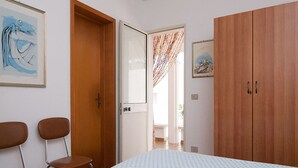 A bedroom with a bed, two chairs, a wardrobe, and a door leading to another room. - HOUSE OF THE DUNES - DONNALUCATA (Donnalucata)