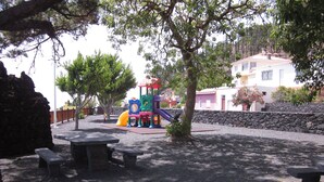 A playground with a slide and climbing structures, surrounded by picnic tables and trees. - Cottage on a quiet place, ideal for rest (Fuencaliente de La Palma)