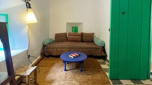 A room with a patterned sofa, a round coffee table, a green door, and a hanging light fixture.