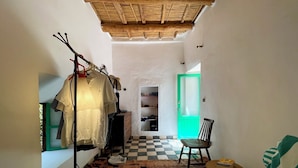 A bedroom with a checkered floor, a bed with a striped blanket, a chair, a wardrobe, and a green door leading to a bathroom.