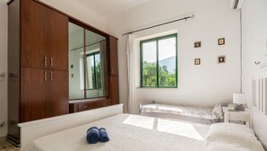 Un dormitorio con una cama grande, un armario, una ventana con vistas y una mesita de noche pequeña.