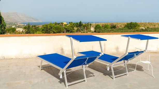 Una terraza con mesas y sillas azules, con vistas a un paisaje costero con montañas y vegetación.