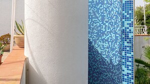 Esquina de un edificio con una pared blanca texturizada y una zona de ducha con azulejos azules.