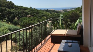 Un balcón con vistas a un paisaje costero, zona de estar con cojines y una pequeña mesa.