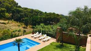 Una piscina con sillones de descanso, rodeada de césped cuidado y árboles.