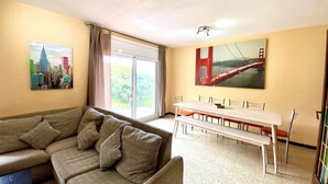 Una sala de estar con un sofá, una mesa de comedor con bancos y dos cuadros en las paredes.
