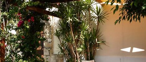 An outdoor patio with a wooden pergola, potted plants, a table with chairs, and a stone wall.