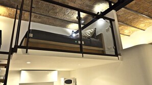 A loft-style bedroom with a bed, a small kitchenette, and a view of the city through a large window. - Quiet luxury apartment in the middle of Rome historical center. (Roma)