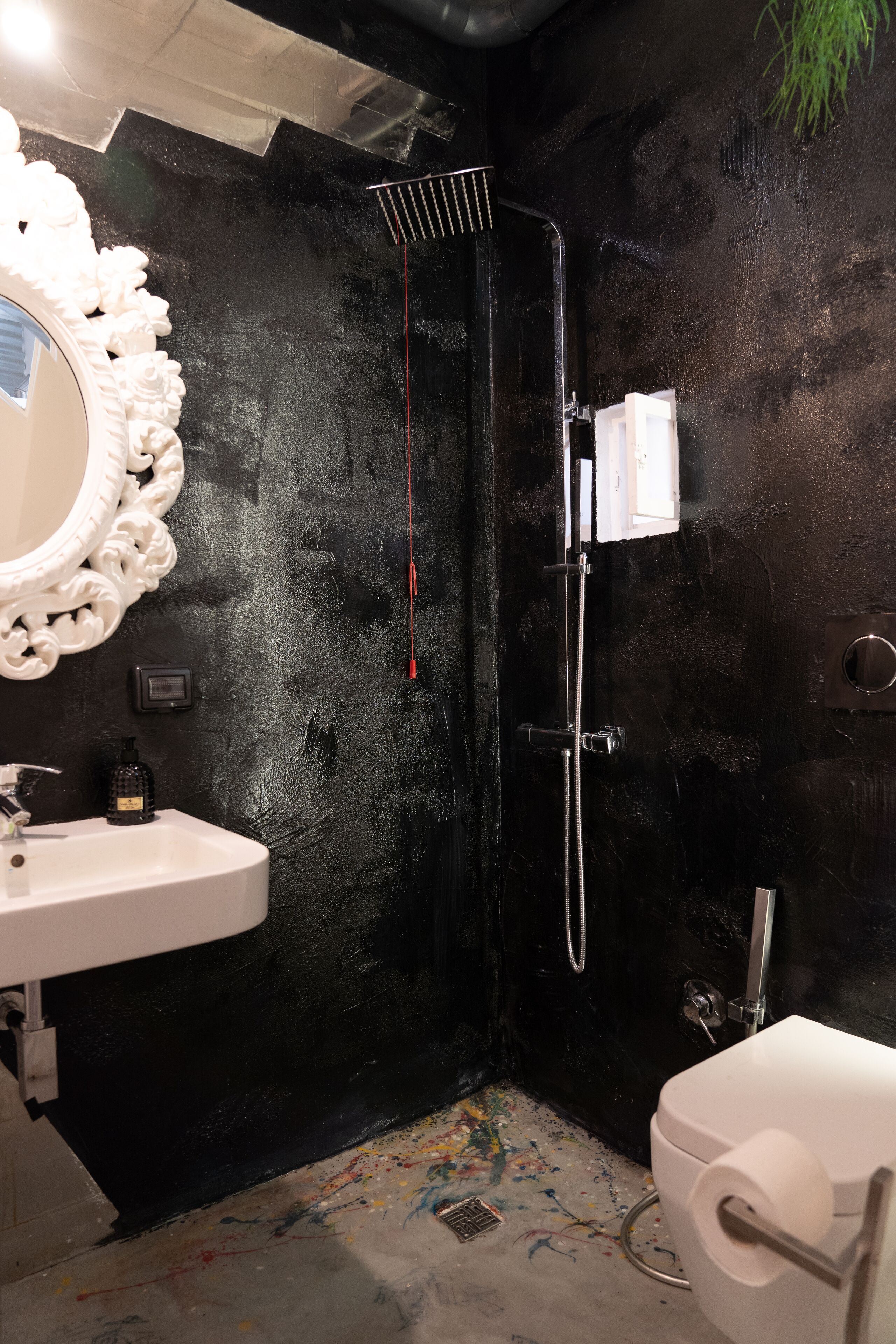 A bathroom with a black wall, a white sink, a mirror, and a shower.