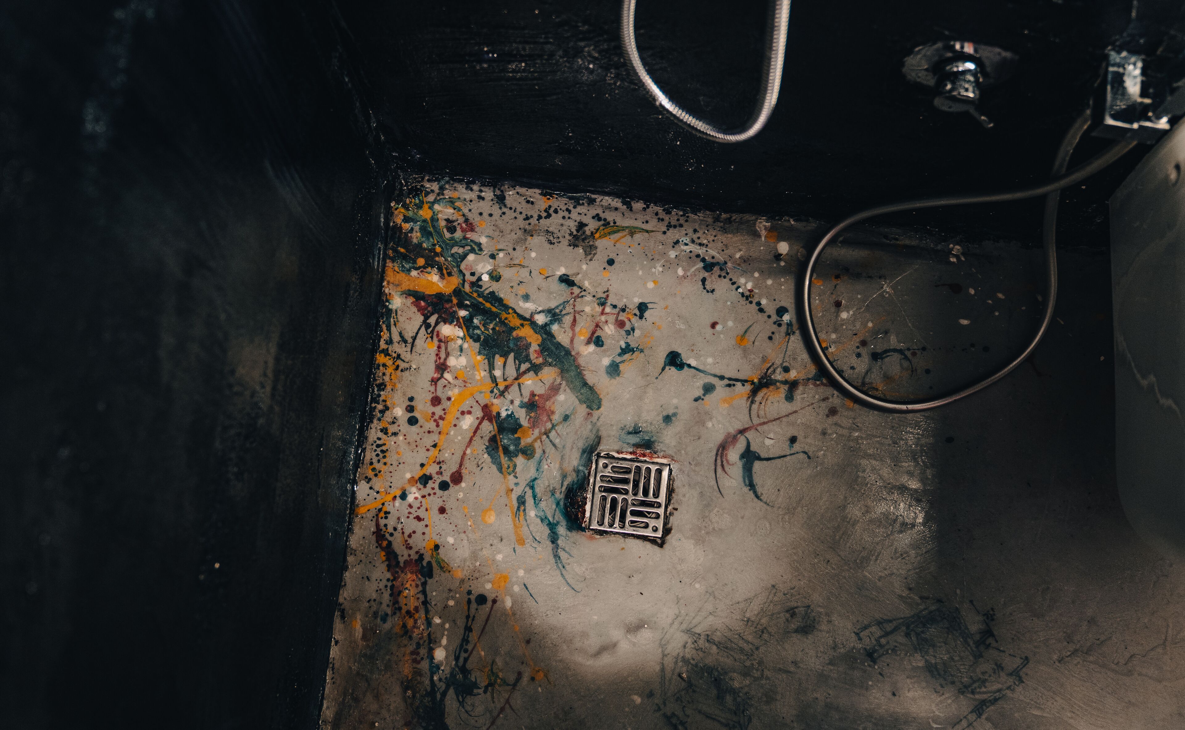 Une surface métallique avec un couvercle d’évacuation et des éclaboussures de peinture dispersées.