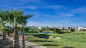 A golf course with palm trees, a pond, and a row of buildings in the background. - Front line views over the golf course (Roldan)