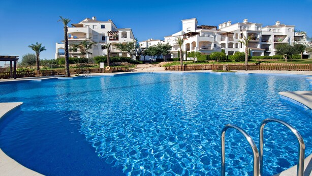 A clear blue swimming pool with metal railings, surrounded by white buildings with balconies and palm trees. - Front line views over the golf course (Roldan)