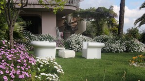 A garden with white planters and flowers, a curved building, and a palm tree. - APARTMENT IN VILLA WITH POOL IN THE SALT, HEATED, SPECTACULAR VIEW !!! (SANT'OMERO)