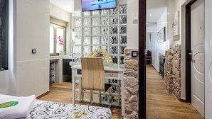 A modern hotel room with a large TV, a glass cabinet with shoes, a wooden chair, and a stone wall. - Holiday Rental Salamanca 4pax WIFI and PARKING / OFFERS end of season (Salamanca)