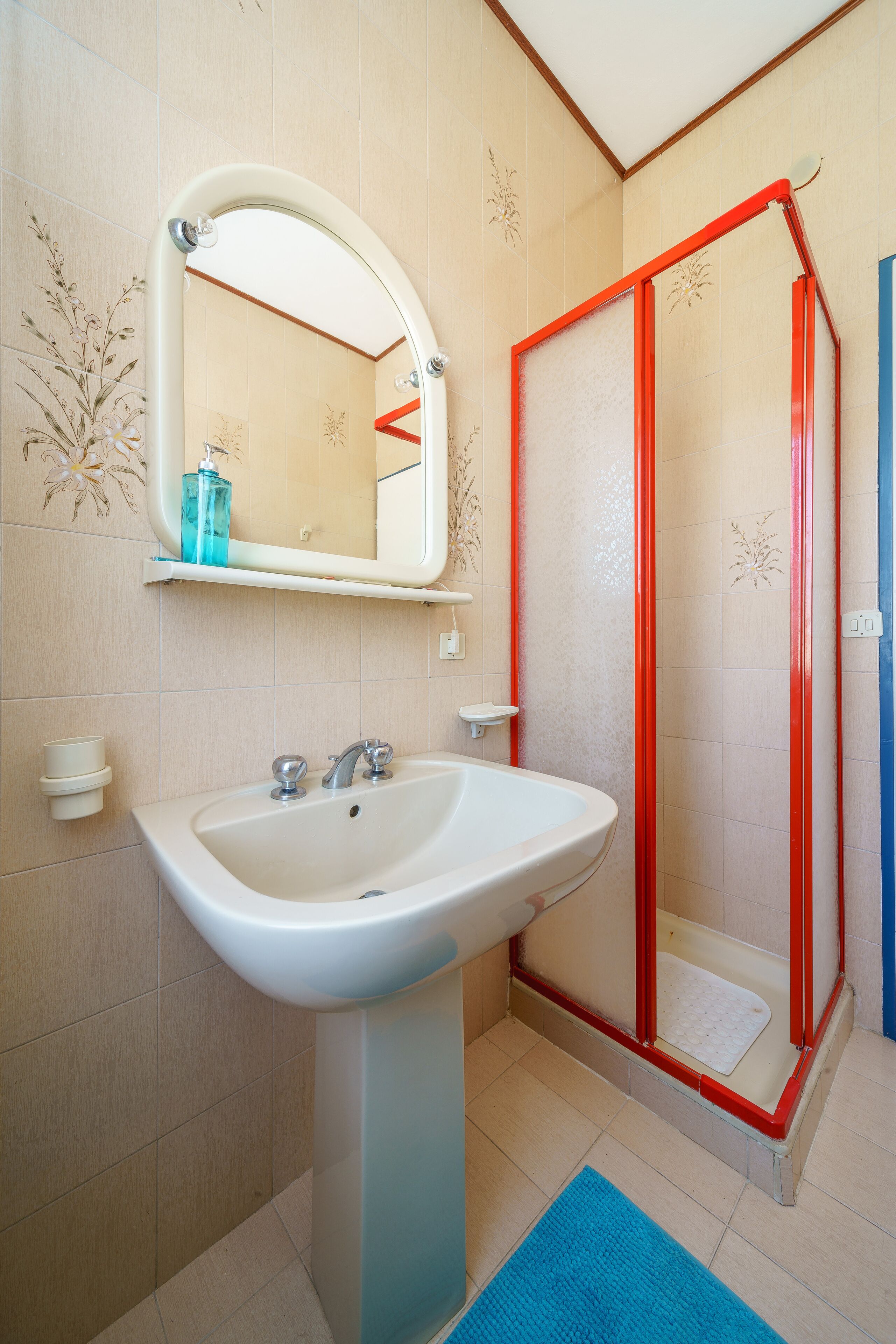 A bathroom with a white sink, a mirror, and a red-framed shower enclosure.