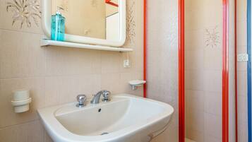 A bathroom with a white sink, a mirror, and a red-framed shower enclosure.