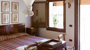 A bedroom with a bed, a wooden desk, a chair, a window with a view of greenery, and framed artwork on the wall. - In September VENICE by train DOLOMITES by car in VENETO 9 Unesco sites 6 p (Cinto Euganeo)