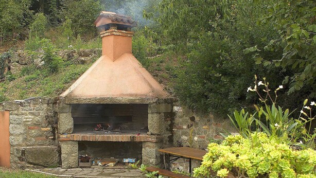 An outdoor stone-built wood-fired oven with a chimney, surrounded by greenery and a wooden bench. - In September VENICE by train DOLOMITES by car in VENETO 9 Unesco sites 6 p (Cinto Euganeo)