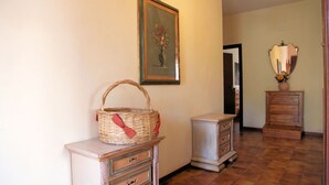 A hallway with a wicker basket on a dresser, a framed painting on the wall, and a mirror above a dresser.