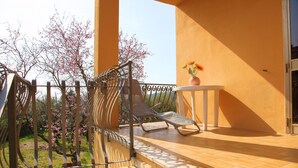 A balcony with two lounge chairs, a small table with a vase of flowers, and a view of blooming trees.