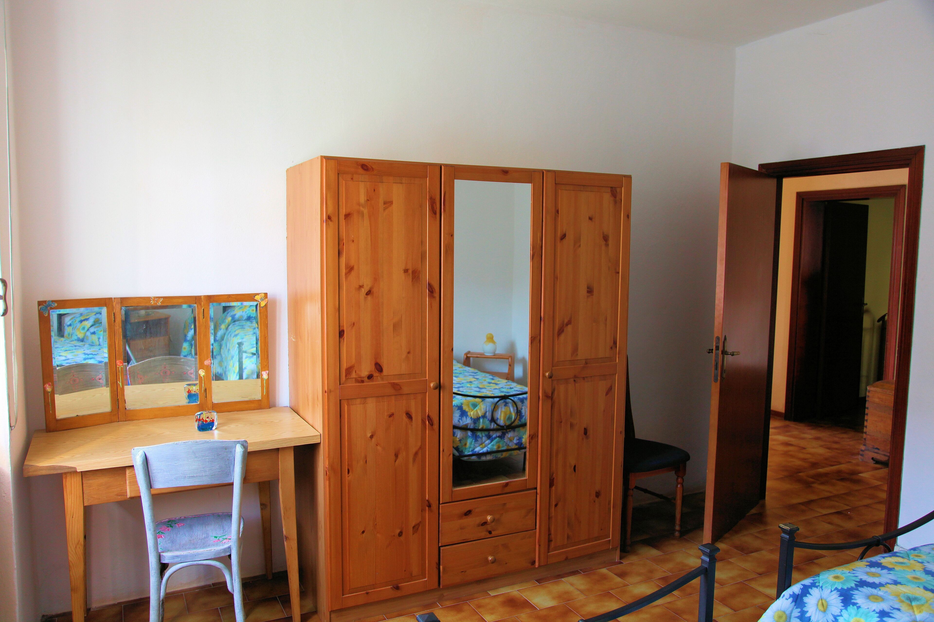 A bedroom with a wooden wardrobe, a desk, and a chair.