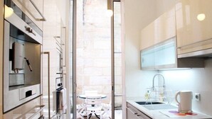 A modern kitchen with stainless steel appliances, a white countertop, and a small dining area with a table and chairs. - Luxury, spacious, patio, near public gardens (Bordeaux)