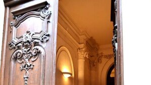 A wooden door with ornate carvings and a brass plate, leading to a staircase with a light fixture above. - Luxury, spacious, patio, near public gardens (Bordeaux)