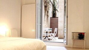 A bedroom with a bed, a bedside table, a chair, and a sliding glass door leading to an outdoor area with a table and chairs. - Luxury, spacious, patio, near public gardens (Bordeaux)
