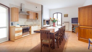 A spacious kitchen with wooden cabinets, a dining table, chairs, a stove, and a TV. - TABACHERA x10 Country House Sirmione GARDA LAKE (pozzolengo)