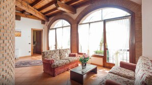 A spacious living room with a red sofa, a coffee table, and large arched windows with curtains. - TABACHERA x10 Country House Sirmione GARDA LAKE (pozzolengo)