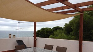 A covered outdoor patio with a table and chairs, overlooking a body of water and greenery.